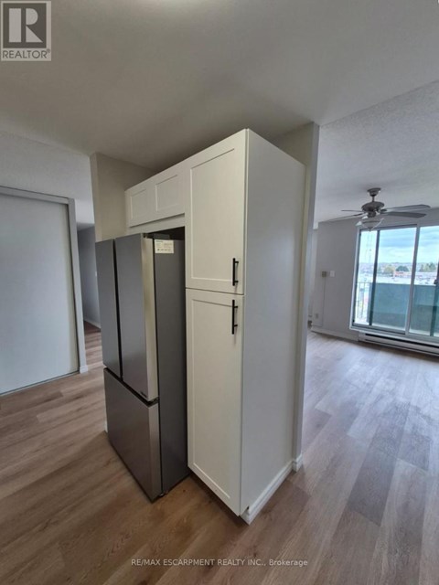 A white refrigerator stands in a room with wooden flooring and a ceiling fan.
