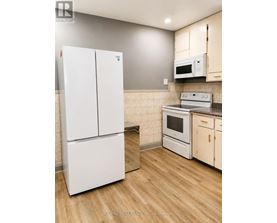 A white refrigerator stands in a kitchen with wooden floors and white cabinets.