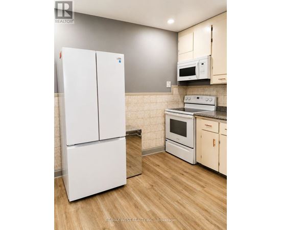 A white refrigerator stands in a kitchen with wooden floors and white cabinets.