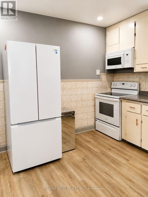 A white refrigerator stands in a kitchen with wooden floors and white cabinets.