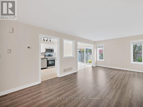 A spacious room with wooden flooring and a kitchen area visible through the open door.