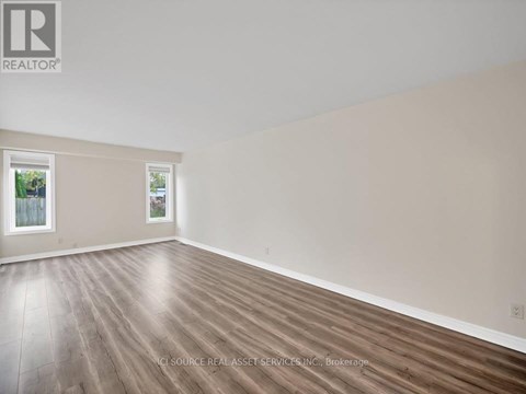 A room with wooden flooring and a window showing a fence and trees outside.
