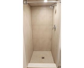 A white tiled shower stall with a drain in the middle.