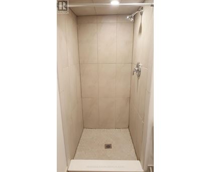 A white tiled shower stall with a drain in the middle.