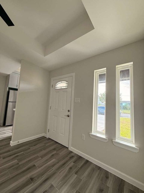 A room with a white door and two windows with light coming through.