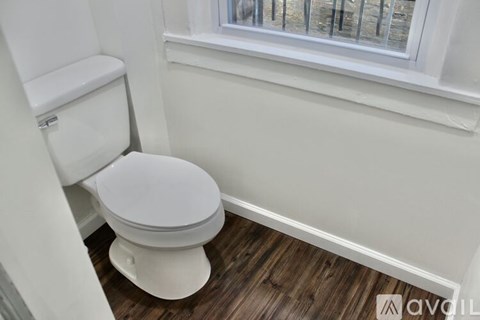 A white toilet in a small room with wooden flooring and a window.