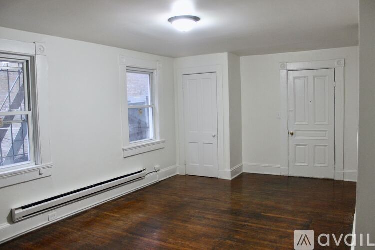 A room with wooden floors and white walls, featuring a window, a door, and a radiator.