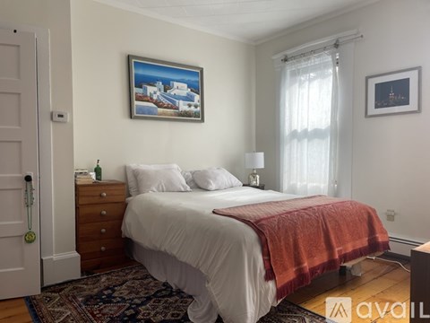 A bedroom with a bed, a dresser, a painting, and a window.
