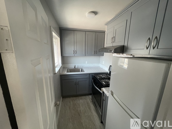 A kitchen with a white refrigerator, grey cabinets, and a black stove top oven.