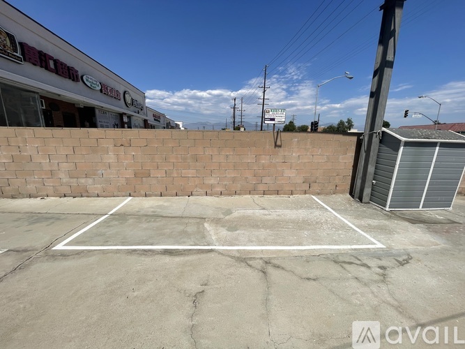 A tennis court is located in front of a brick wall and a building with a sign that reads "AVAILABLE".