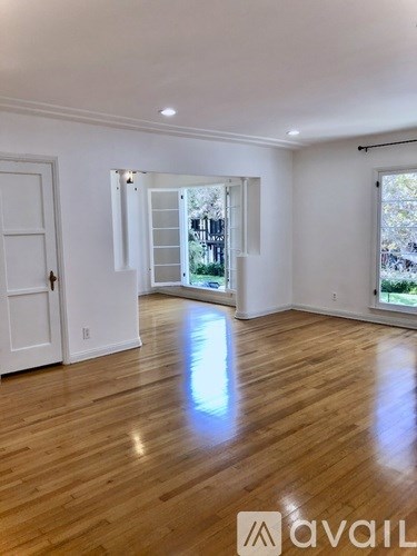 A spacious room with wooden flooring and white walls, with a door and a window.