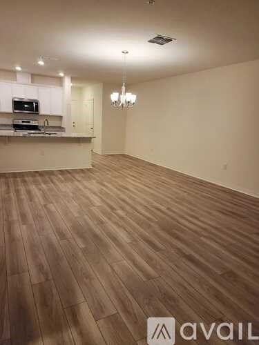 A spacious room with wooden flooring and a kitchen area with white cabinets.
