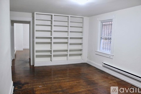 A room with a wooden floor and a window with bars on it.
