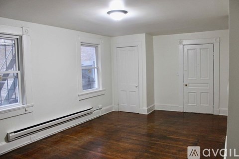 A room with wood floors and white walls has a window and two doors.