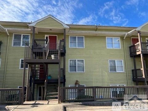 A two-story apartment building with a balcony and a red door.