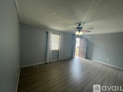 A room with a ceiling fan and light, wooden floors, and a door leading to another room.