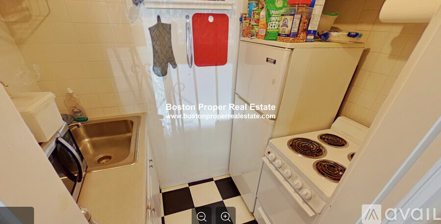 A small kitchen with a white fridge and a black and white checkered floor.