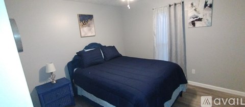 A bedroom with a blue bedspread and a white lamp on a side table.