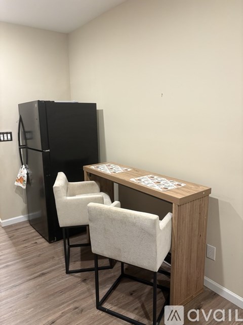 A black fridge sits next to a wooden table with two chairs.