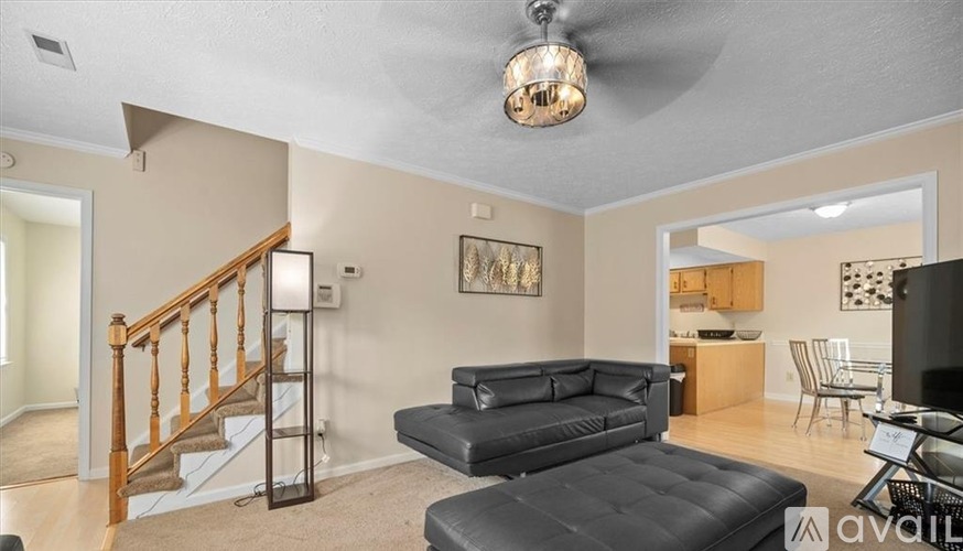A living room with a black leather couch and a wooden staircase.