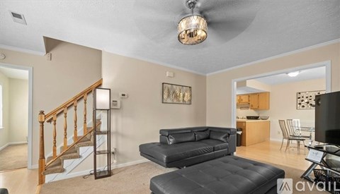 A living room with a black leather couch and a wooden staircase.