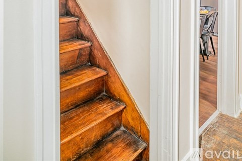 A wooden staircase with a white wall on the left and a doorway leading to a dining area on the right.