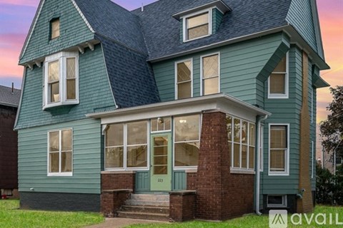 A house with a greenish exterior and a brick base is shown.