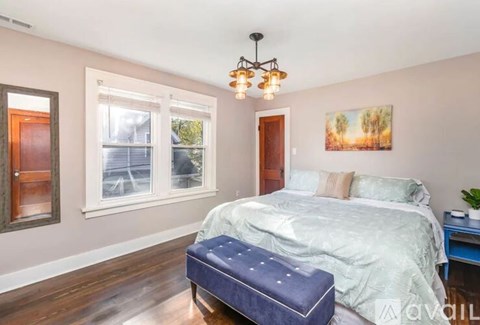 A bedroom with a bed, a bench, and a painting on the wall.