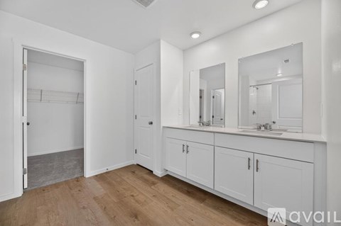 A spacious bathroom with wooden floors and white walls.