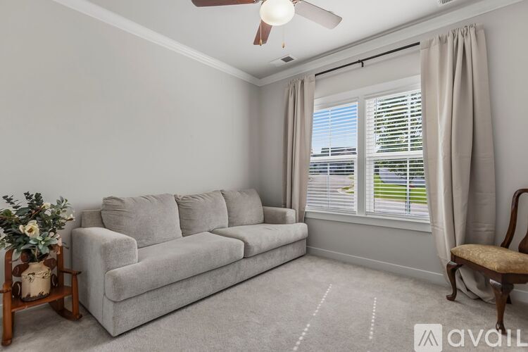 A living room with a grey couch, a fan, and a window with curtains.