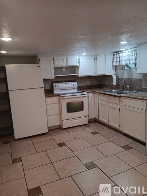 A kitchen with white appliances and brown tiled floors.