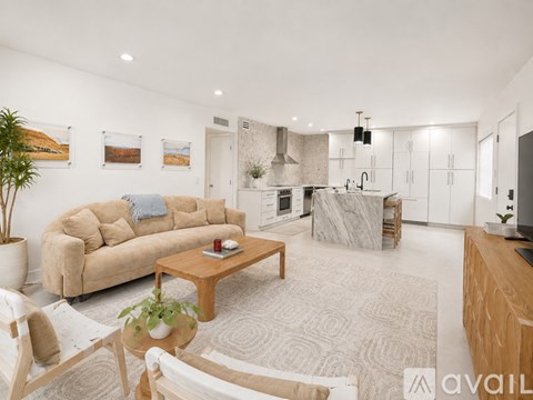 A living room with a couch, coffee table, and a kitchen area in the background.