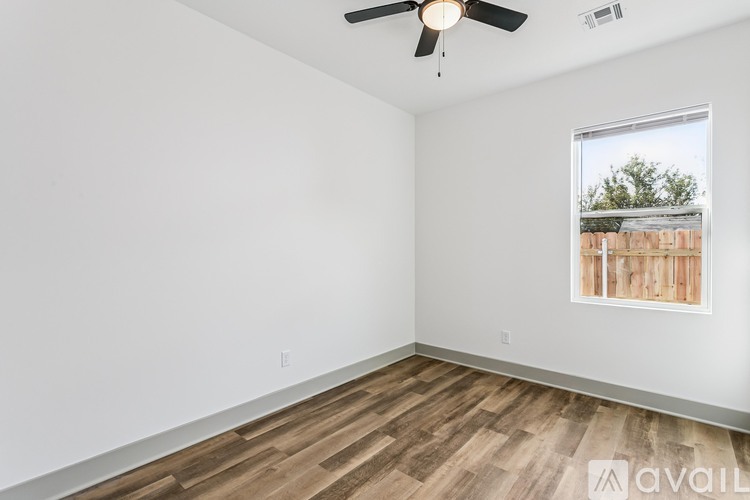 A room with a ceiling fan and a window showing a fence and trees outside.