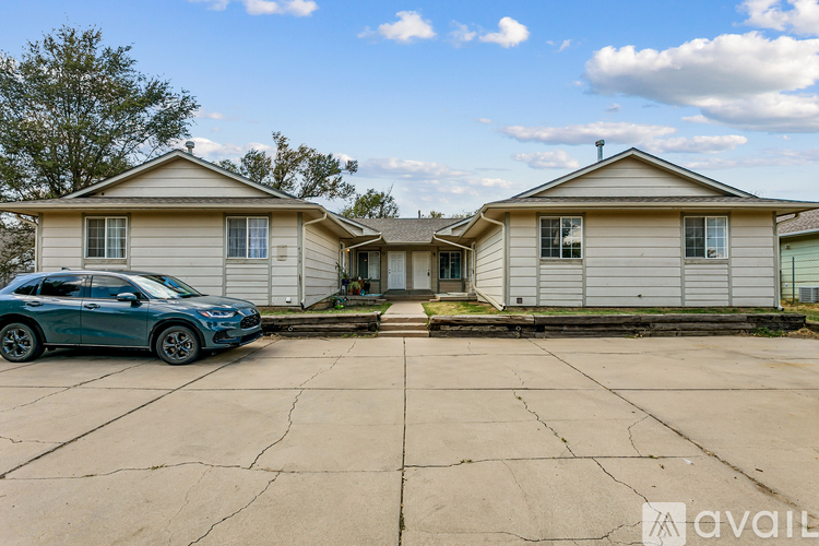 A blue car is parked in front of a two-story house.