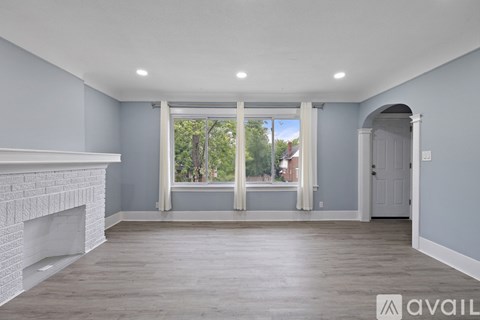 A spacious room with a fireplace on the left and a large window with a view of trees and a building in the distance.