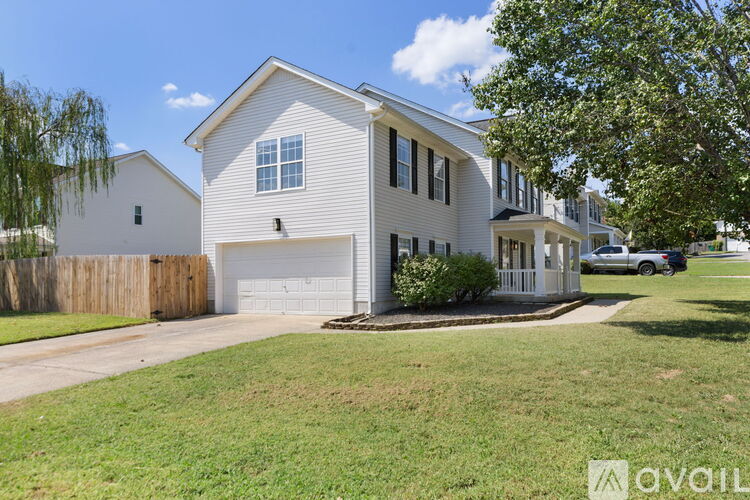 A white house with a garage is surrounded by a green lawn and a wooden fence.