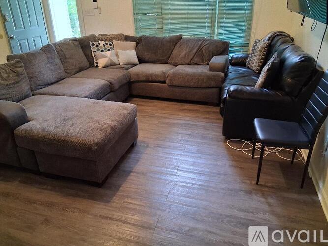 A living room with a brown couch, a black leather couch, and a brown ottoman.