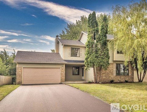A two-story house with a garage is surrounded by trees and has a driveway leading to the front door.