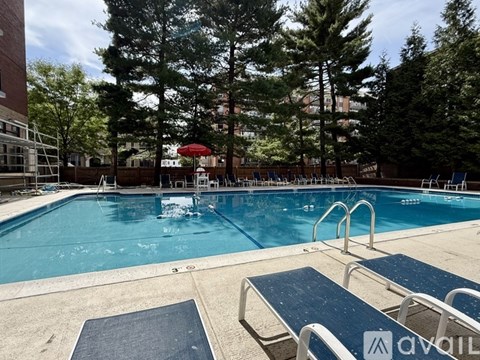 A pool with a blue tiled edge and a red umbrella in the distance.