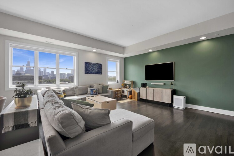 A living room with a grey couch and a large window overlooking a cityscape.