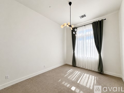 A room with a carpeted floor, a window with curtains, and a chandelier.