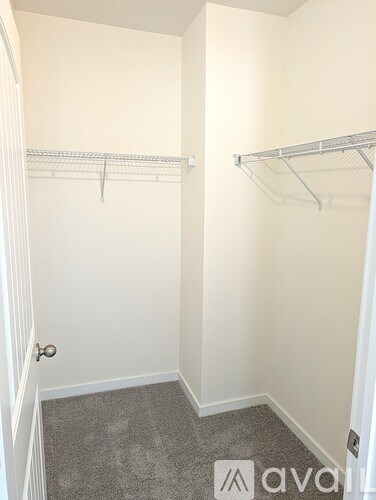 A small, empty bedroom with a carpeted floor and two metal racks on the wall.