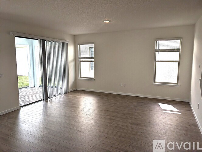A spacious room with wooden flooring and two windows.
