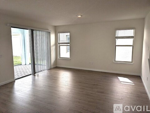 A spacious room with wooden flooring and two windows.