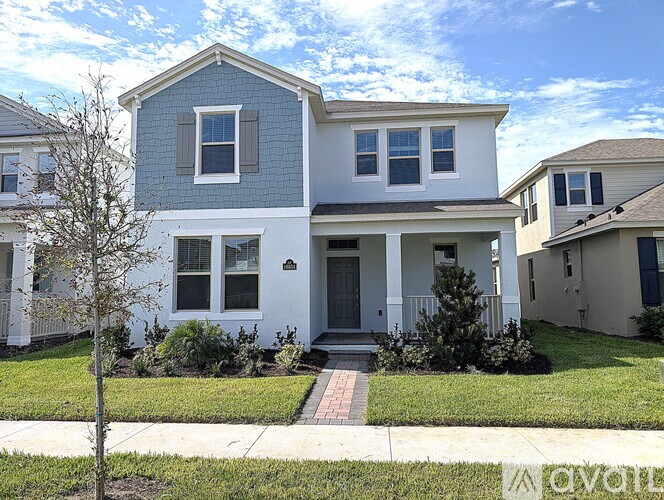 A two-story house with a front porch and a tree in front.