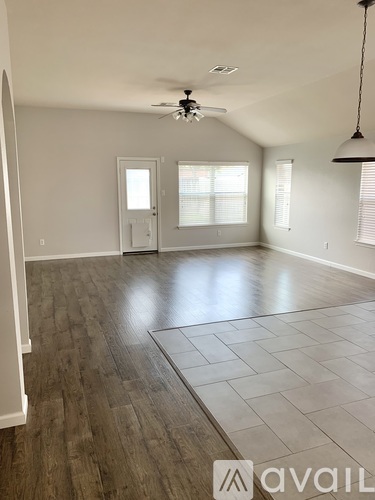 A spacious room with a ceiling fan and light, hardwood flooring, and a rug on the floor.
