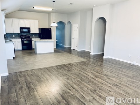 A spacious kitchen with a black oven and microwave, white cabinets, and a wooden floor.