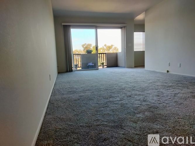 A spacious room with a carpeted floor and a sliding glass door leading to a balcony.