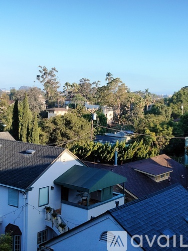 A white house with a green awning is in the foreground of a tree-filled residential area.