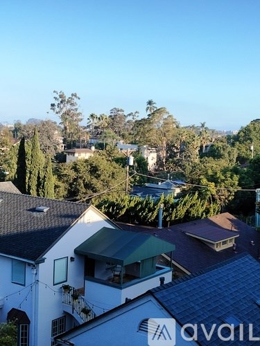 A white house with a green awning is in the foreground of a tree-filled residential area.